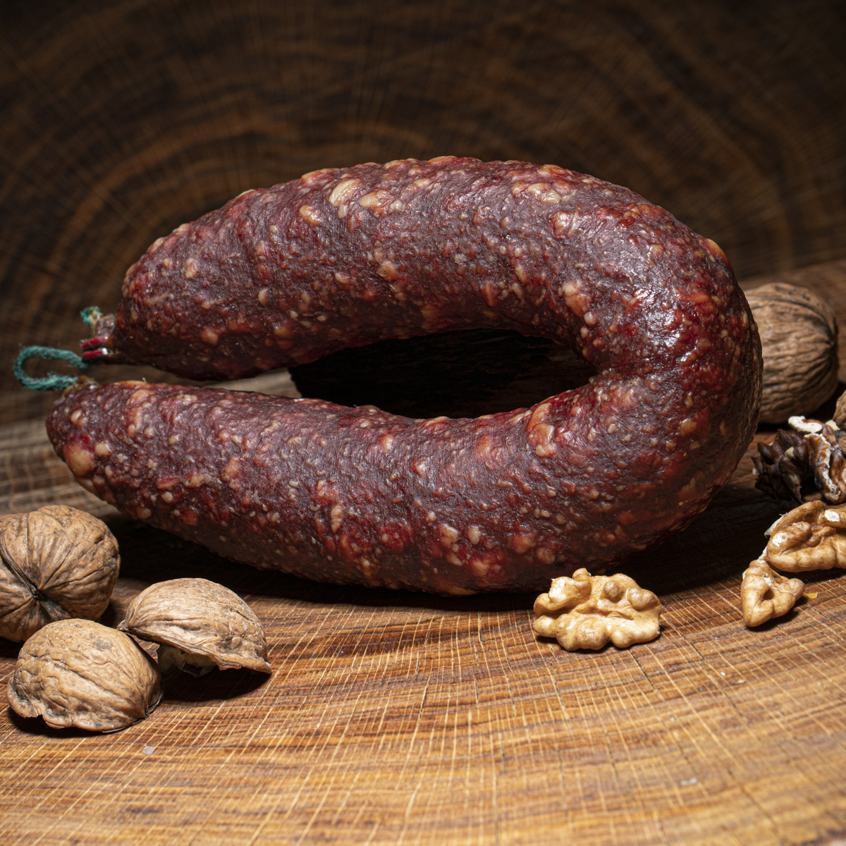Walnusssalami gebogen auf einem Holztisch mit Walnüssen darauf als Deko.