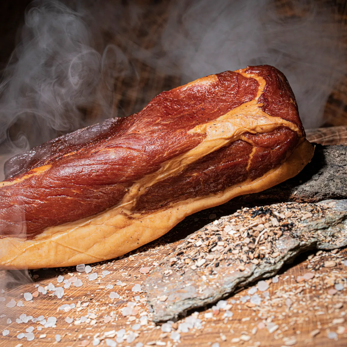 Mangalitza Wollschwein Schinken mit Rauch im Hintergrund mit Holzspähnen Deko.