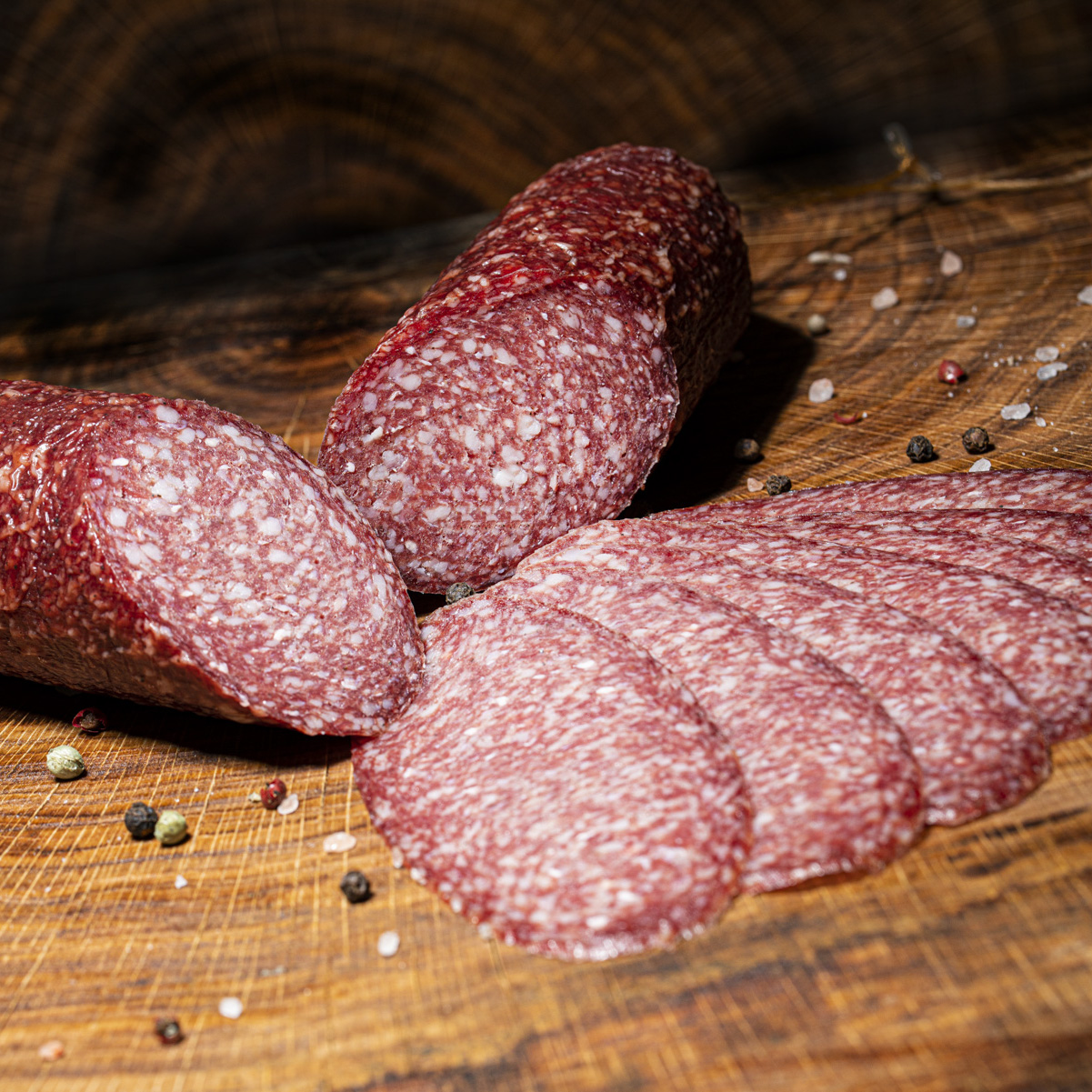 Hauseigene Salami in klein und aufgeschnitten auf einem Holztisch.